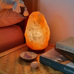 Himalayan salt lamp glowing on a wicker bedside table next to books and a small dish