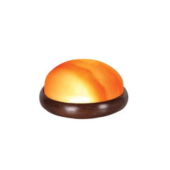 Dome-shaped Himalayan salt massage stone glowing amber in a wooden bowl against a white background