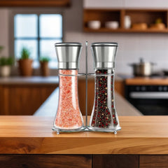 Glass salt and pepper grinder set on a wooden kitchen counter, one filled with pink Himalayan salt