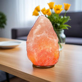 Large Himalayan salt lamp glowing on a wooden coffee table beside yellow tulips