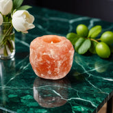 Himalayan salt candle holder with a lit tealight on a green marble table beside white flowers and limes