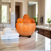 Fire bowl Himalayan salt lamp filled with round massage-ball salt stones on a marble bathroom counter beside towels