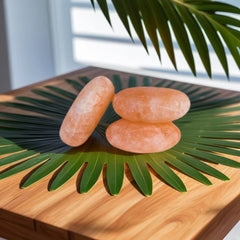 Three oval polished Himalayan salt massage stones on a palm leaf atop a wooden table
