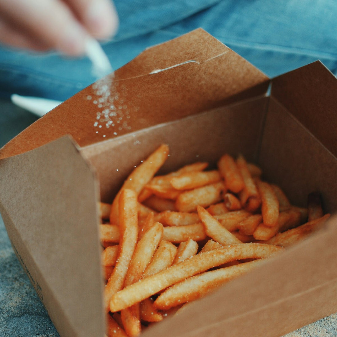 Hand sprinkling salt over freshly cooked fries, seasoning food with pink salt