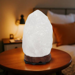 White crystal Himalayan salt lamp glowing on a bedroom side table beside a bed with orange cushions