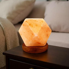 Diamond-cut Himalayan salt USB lamp glowing on a dark side table beside a cream sofa
