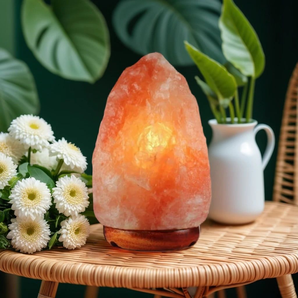 Himalayan salt lamp glowing on a rattan table beside white chrysanthemums and a jug of greenery