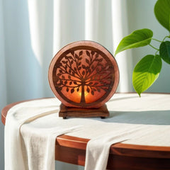 Round tree-of-life wood and salt lamp glowing amber on a table with a white tablecloth beside a plant