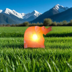 Elephant-shaped Himalayan salt lamp glowing in a green field with snow-capped mountains in the background