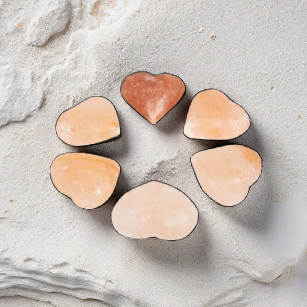 Six heart-shaped Himalayan salt massage stones arranged in a circle on a textured stone surface