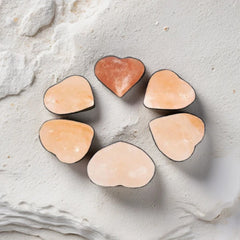 Six heart-shaped Himalayan salt massage stones arranged in a circle on a textured stone surface