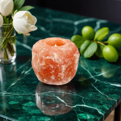 Himalayan salt candle holder with a lit tealight on a green marble table beside white flowers and limes