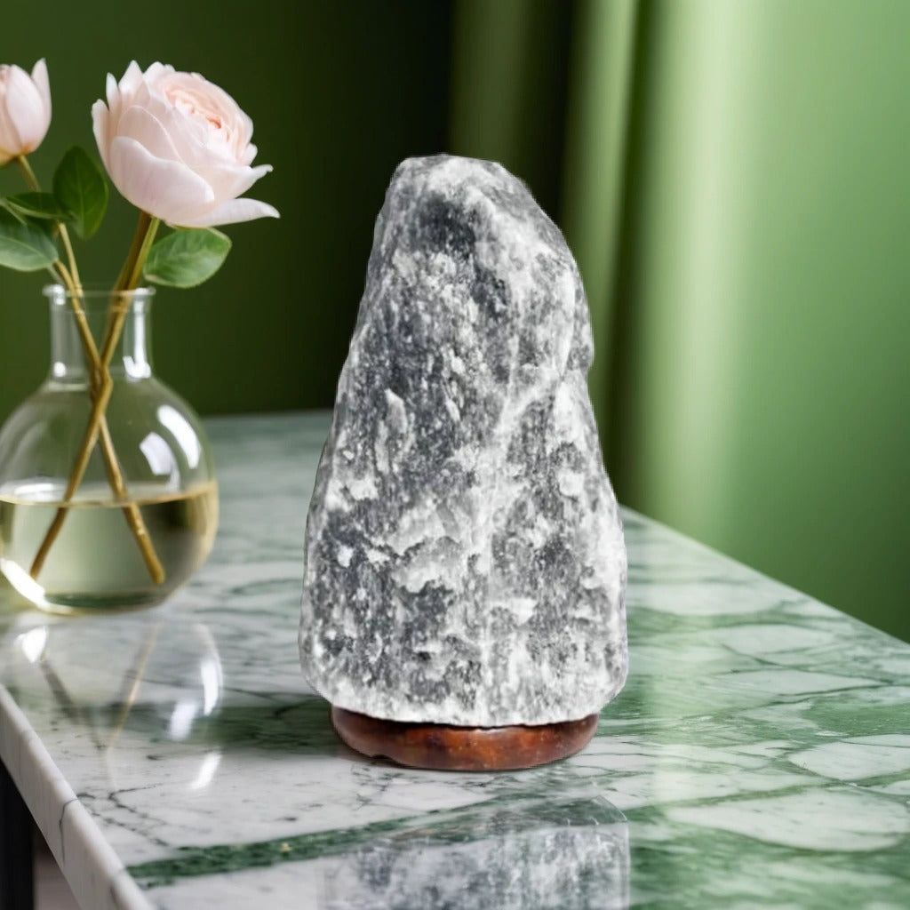 Grey Himalayan salt lamp on a green marble counter beside a vase of pink roses