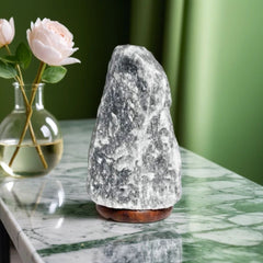 Grey Himalayan salt lamp on a green marble counter beside a vase of pink roses
