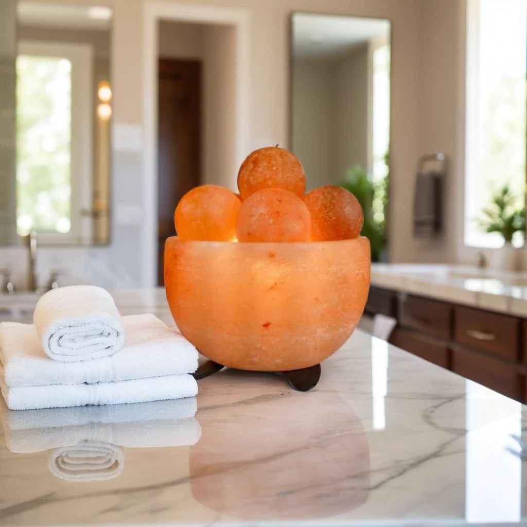 Fire bowl Himalayan salt lamp filled with round massage-ball salt stones on a marble bathroom counter beside towels