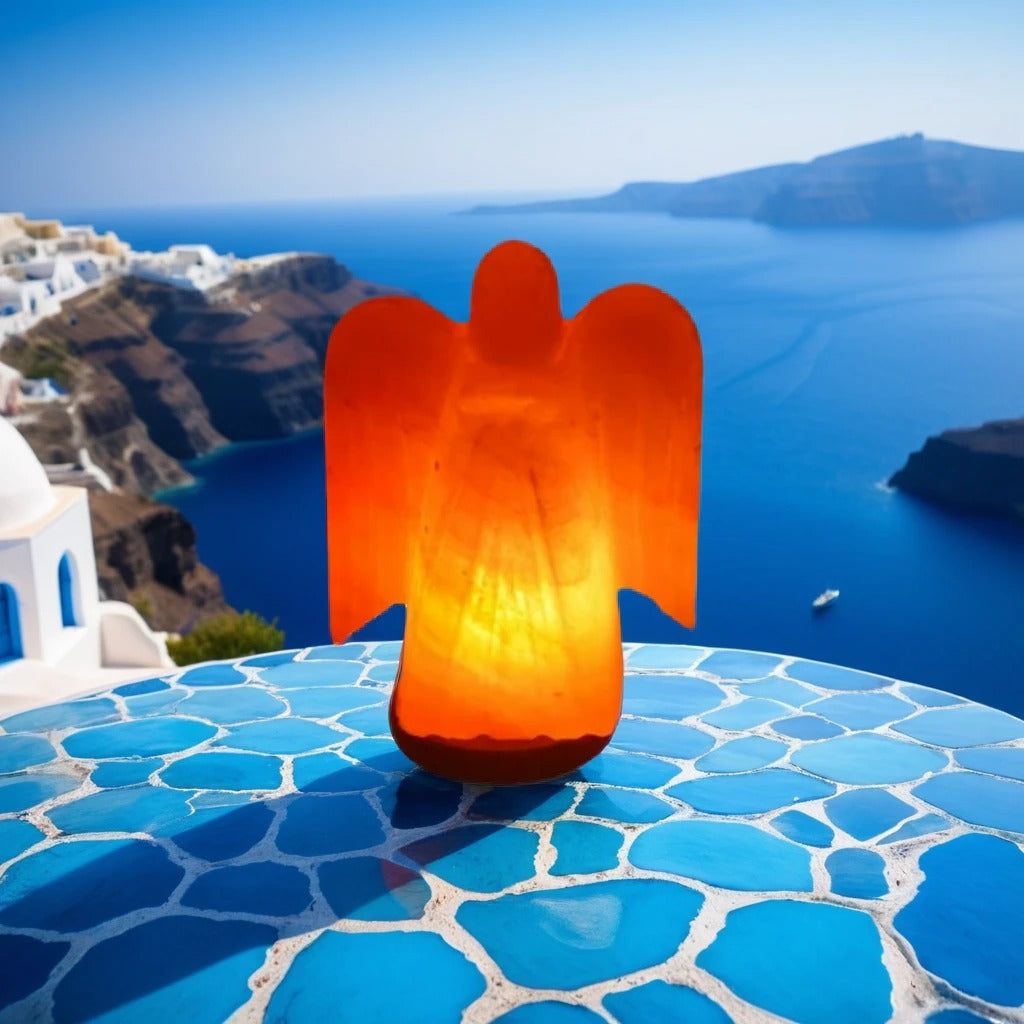 Angel-shaped Himalayan salt lamp lit on a blue tiled table with a coastal view behind it