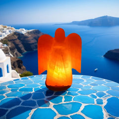 Angel-shaped Himalayan salt lamp lit on a blue tiled table with a coastal view behind it