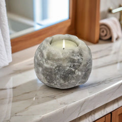 Grey Himalayan salt candle holder with a lit tealight on a marble bathroom counter