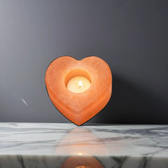 Heart-shaped Himalayan salt candle holder with a lit tealight, standing on a marble surface