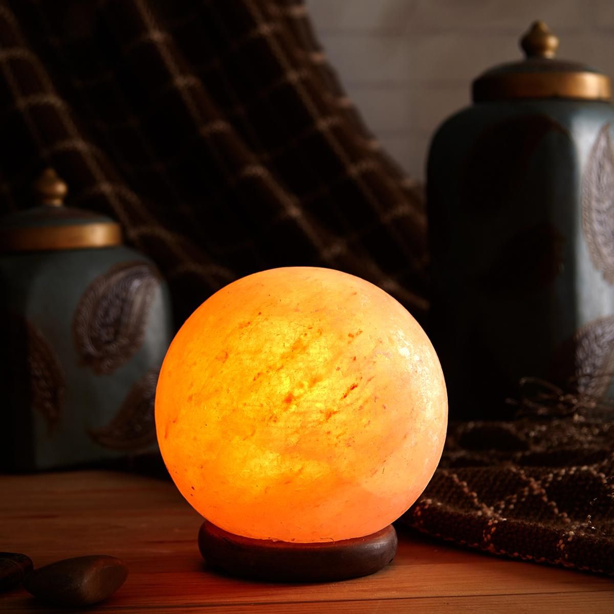 Spherical Himalayan salt lamp glowing amber on a wooden table beside decorative ceramic jars